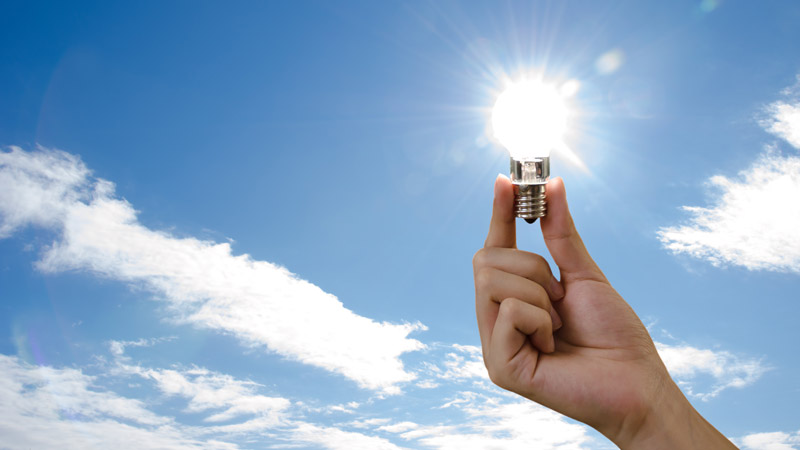 Light bulb being held up to the sky shining like the sun